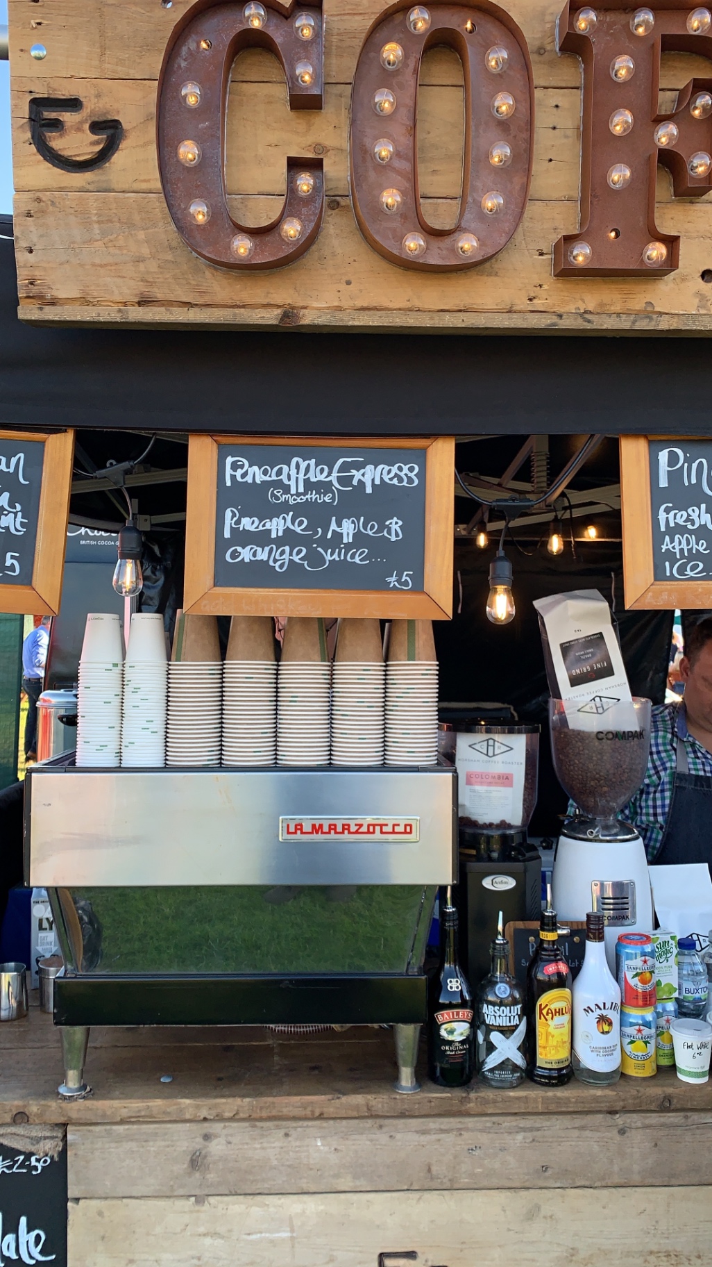 Close-up of a La Marzocco espresso machine beneath the rustic marquee COFFEE sign