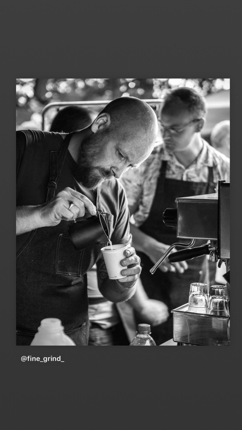 Black and white photo of a Fine Grind barista pouring latte art